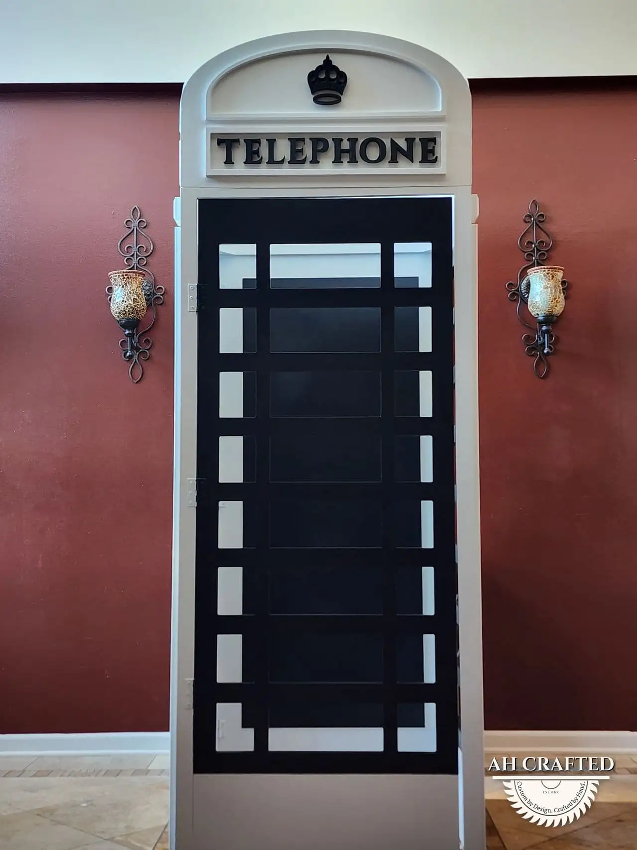 The finished telephone box head-on against a maroon wall, framed by two sconces.